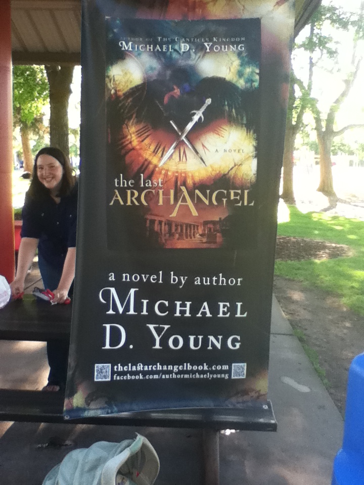 Michael D. Young’s wife standing beside a life-size promotional poster for The Last Archangel
